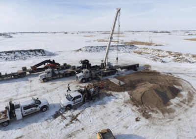 A crane operates on a snow-covered site, moving a pile of dirt amidst a winter landscape